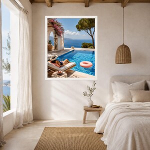 May include: A framed wall art print depicting a Mediterranean scene with a person lounging on a poolside daybed, a pink inflatable ring in the blue water, a stone archway with pink flowers, and a distant sea view under a clear blue sky.