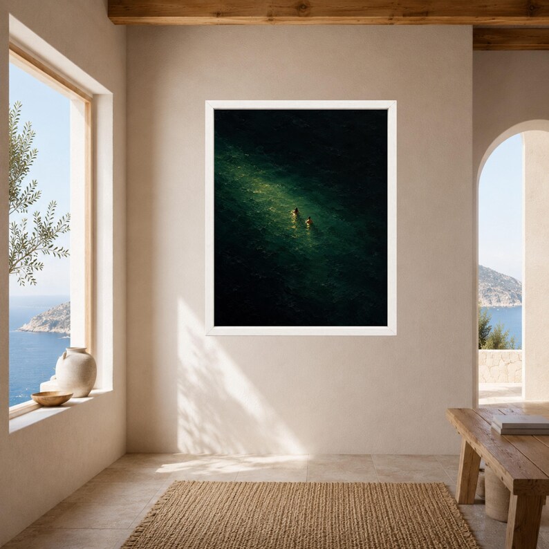 May include: A framed wall art print featuring an aerial view of deep green ocean water with two small figures swimming in a patch of sunlight. The artwork is enclosed in a simple white frame, showcasing a high-contrast scene of dark sea.