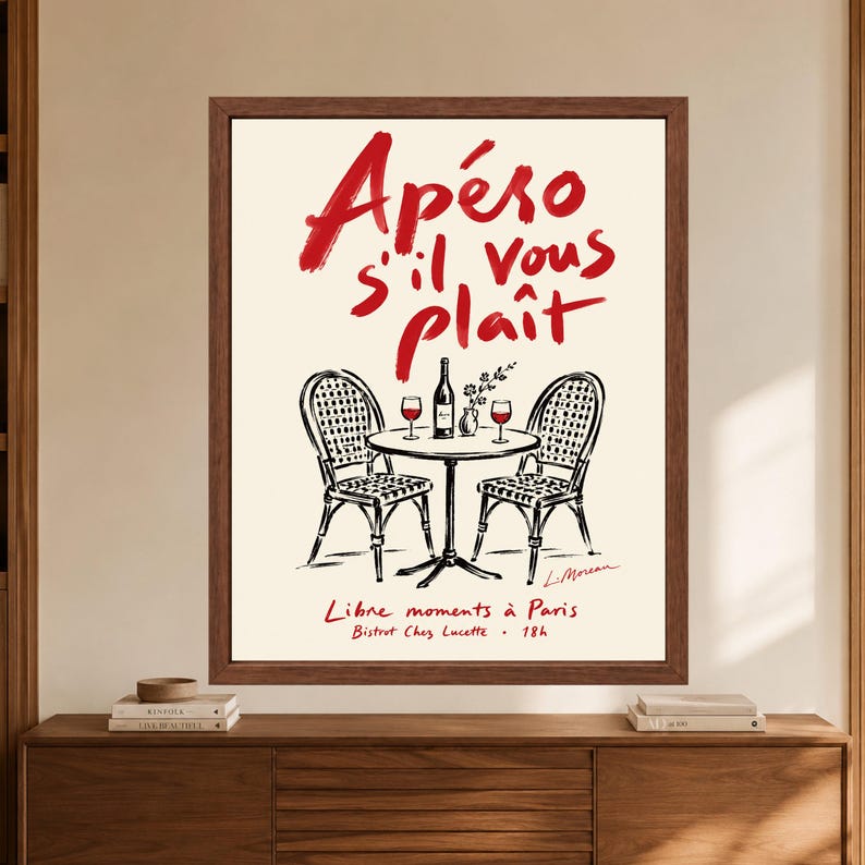 May include: A framed wall art print featuring a cream background with red text reading Ap&eacute;ro s'il vous pla&icirc;t and black line art of a bistro table with two chairs, a wine bottle, and two glasses. Below, red text reads Libre moments &agrave; Paris.