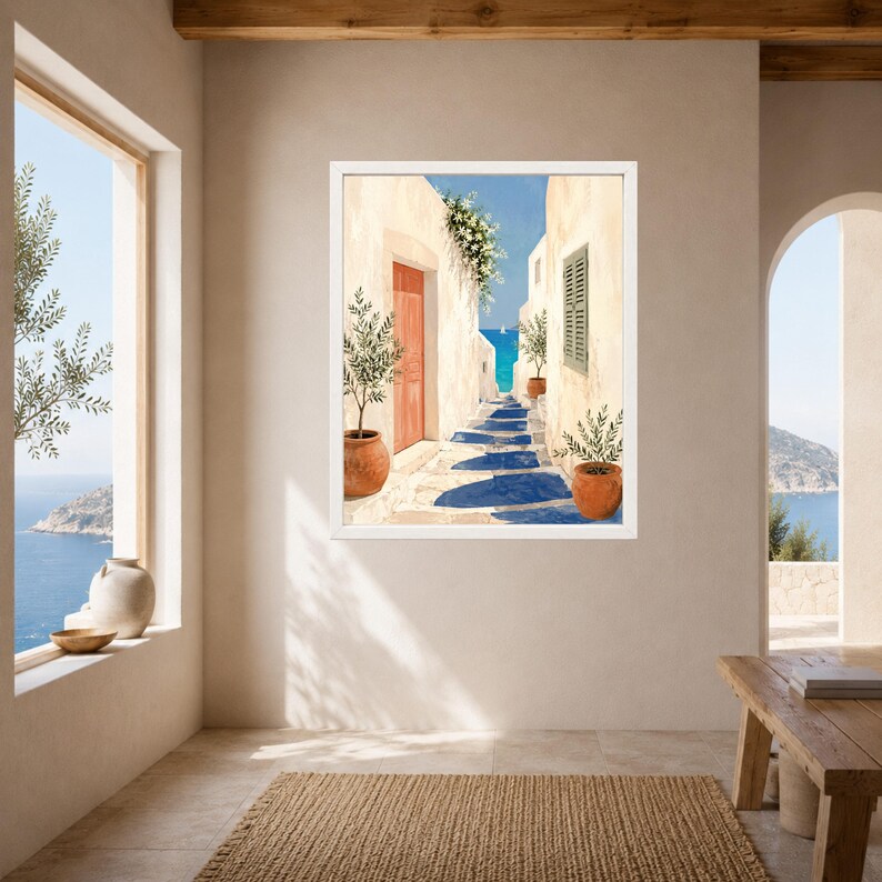 May include: A framed wall art print depicting a narrow Mediterranean alleyway with cream-colored stone walls, a vibrant orange door, terracotta pots containing green olive trees, and a view of the bright blue sea under a clear sky.