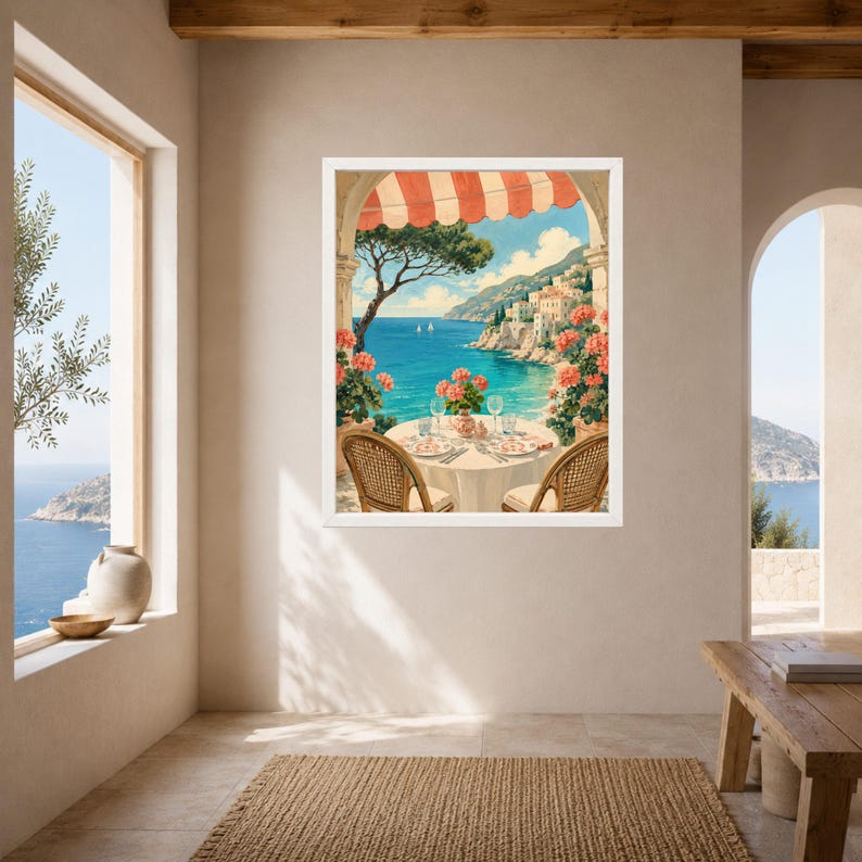 May include: A framed wall art print depicting a coastal Mediterranean scene under a red and white striped awning. The image shows a round table set for two with pink flowers, overlooking a blue sea, distant cliffs, and white hillside buildings.