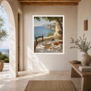 May include: A framed wall art print depicting a Mediterranean coastal scene with a table set for a meal under a tree. The table features a white cloth, plates, a glass carafe, and red tomatoes, overlooking a blue sea and rocky cliffs in the distance.