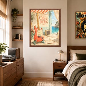 May include: A framed wall art print titled Coastal Chords featuring a coral-coloured electric guitar on a stand, a small amplifier, and a cable on a stone patio overlooking a blue sea. The scene includes a doorway with curtains and a striped awning.