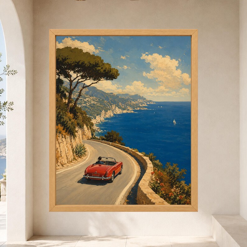 May include: A framed wall art print depicting a red convertible car driving along a winding coastal road. The scene features a deep blue sea, rocky cliffs, green trees, and a bright sky with white clouds, all enclosed in a light wood frame.