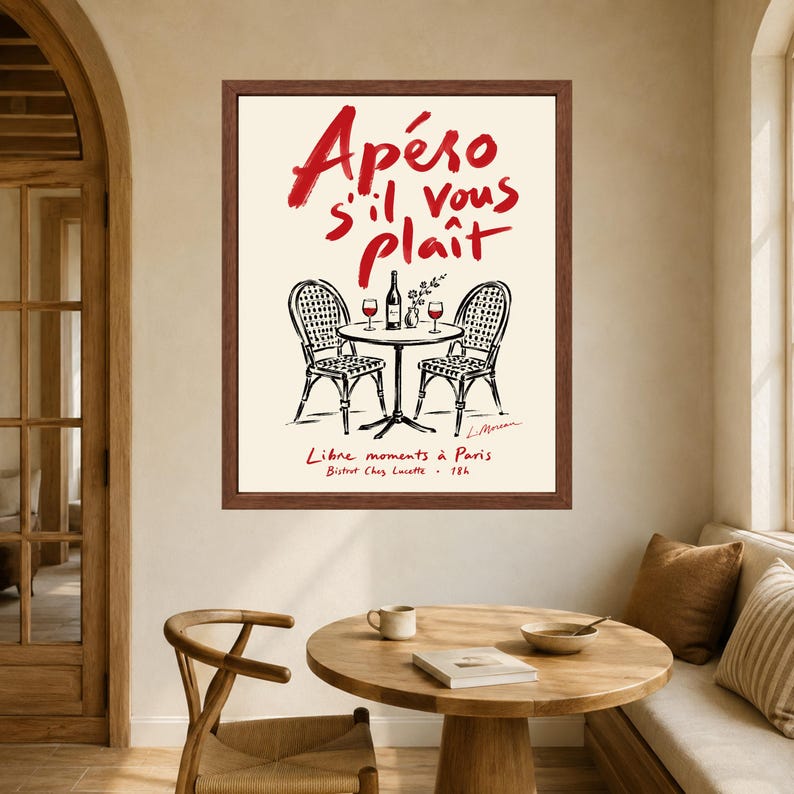 May include: A framed wall art print featuring a cream background with red handwritten text that reads Ap&eacute;ro s'il vous pla&icirc;t. Below the text is a black ink illustration of a bistro table with two chairs, a wine bottle, and two glasses.