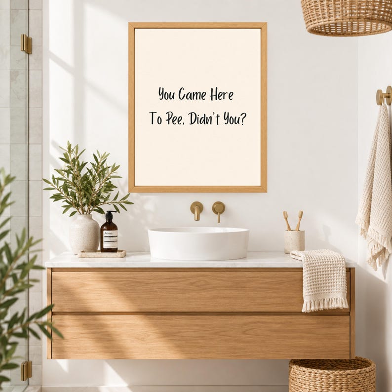 May include: A rectangular wall art piece in a light wood frame featuring a cream-colored background with the black text "You Came Here To Pee, Didn't You?" centered on the print. The artwork is displayed above a white vessel sink in a bathroom.