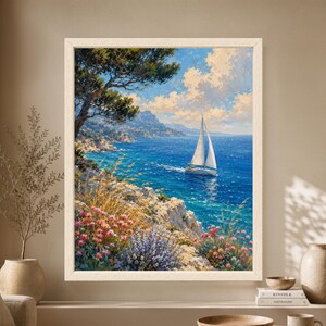 Framed Mediterranean coastal wall art showing a white sailboat on deep blue water below a rocky shoreline with pine trees, pink wildflowers, distant mountains and bright summer clouds.