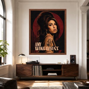 Puede incluir: Una impresi&oacute;n art&iacute;stica enmarcada que presenta un retrato de Amy Winehouse con su caracter&iacute;stico peinado de colmena, delineador de ojos oscuro y pendientes de aro. El fondo es un c&iacute;rculo rojo intenso sobre negro, con el texto AMY WINEHOUSE en beige.