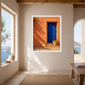 Pu&ograve; includere: Una stampa artistica da parete incorniciata che raffigura una vivace parete in stucco arancione con una porta in legno blu intenso. Un gatto rosso riposa sulla soglia in pietra accanto a un cesto di vimini pieno di limoni gialli e foglie verdi.