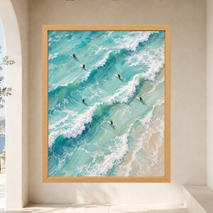 May include: A framed oil painting depicting an aerial view of turquoise ocean waves crashing onto a sandy beach. Several surfers on white surfboards are positioned within the rolling water, captured with visible brushstrokes and white sea foam.