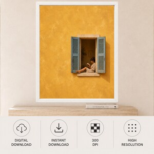 Puede incluir: Una impresi&oacute;n de arte mural enmarcada que muestra una pared de color amarillo mostaza texturizada con una ventana abierta. La ventana tiene contraventanas de lamas azul claro y muestra a una persona sentada en el alf&eacute;izar leyendo un libro.
