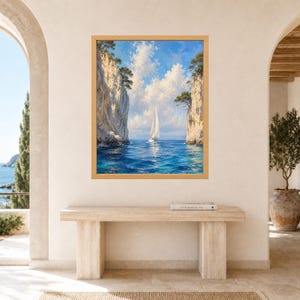 May include: A framed landscape painting depicting a white sailboat navigating through a narrow passage between two tall, rocky cliffs. The scene features deep blue ocean water, a bright blue sky with fluffy white clouds, and green trees.