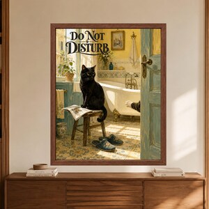 Framed funny black cat bathroom wall art with a cat sitting on a wooden stool over an open newspaper, a second cat paw reaching through a blue door, and large Do Not Disturb lettering in a warm vintage-style bathroom.