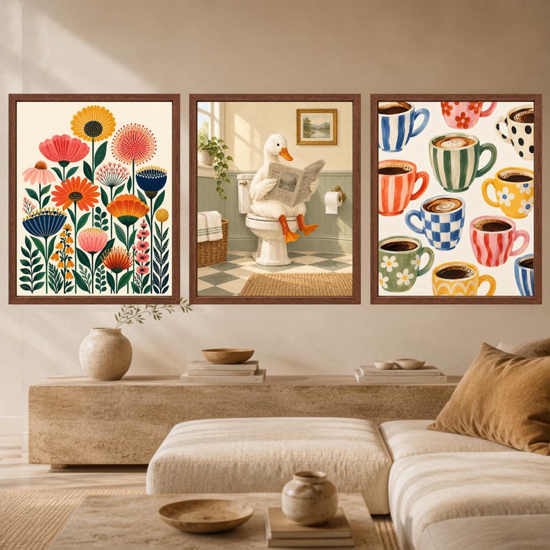 May include: A set of three framed wall art prints. The left print features colorful stylized flowers. The center print shows a white duck sitting on a toilet reading a newspaper. The right print displays a pattern of various coffee mugs.