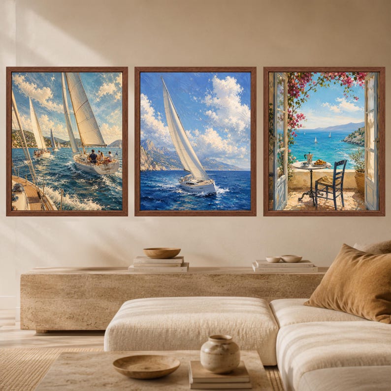 May include: A set of three framed wall art prints. The first two prints depict sailboats on blue water under a cloudy sky. The third print shows a view through an open window onto a balcony with a table, chair, and pink flowers overlooking the sea.