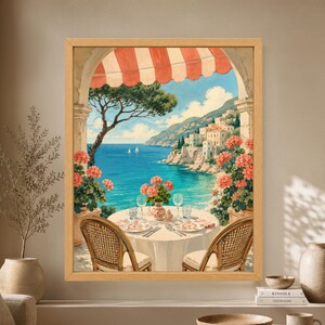 Framed Mediterranean terrace wall art showing a table for two beneath a red striped awning with coral flowers, turquoise sea, sailboats and a sunlit Italian coastal village.
