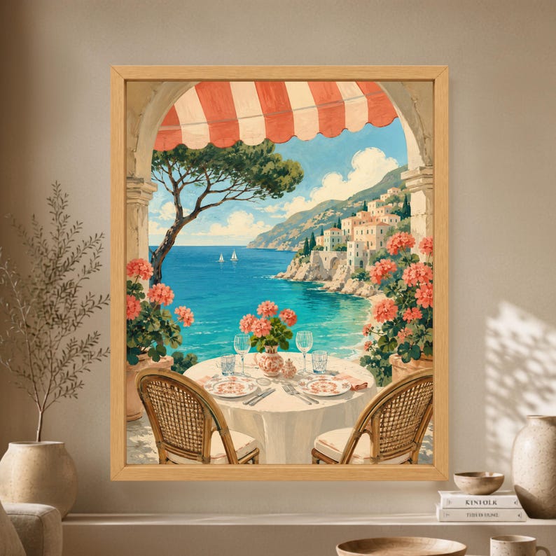 Framed Mediterranean terrace wall art showing a table for two beneath a red striped awning with coral flowers, turquoise sea, sailboats and a sunlit Italian coastal village.