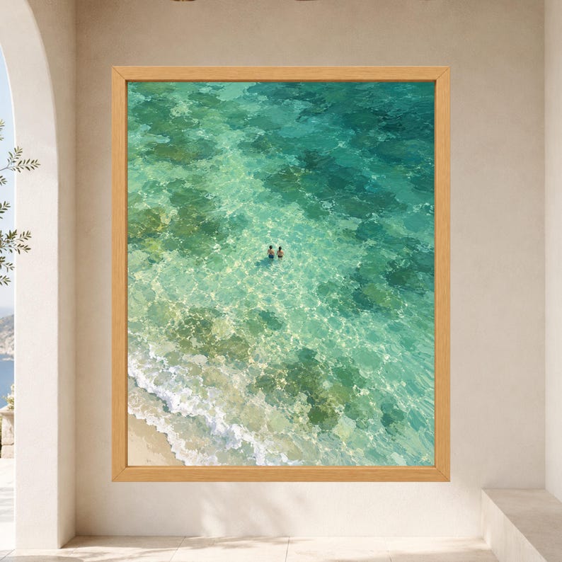 May include: A framed wall art print featuring an aerial view of clear turquoise ocean water with a sandy shoreline and two small figures swimming in the center. The water displays light-refracting patterns and visible rocky seabed textures.