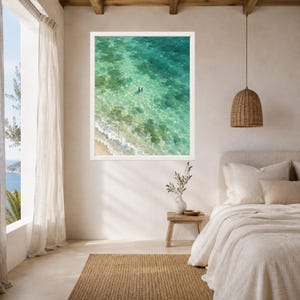 May include: A framed wall art print featuring an aerial view of turquoise ocean water with gentle white waves washing onto a sandy shore. Two small figures are visible swimming in the clear, shallow water, showcasing a vibrant coastal scene.