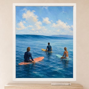 May include: A framed wall art print depicting three individuals on surfboards in the ocean. One person wears a dark long-sleeve top on a coral board, another a dark short-sleeve top on a yellow board, and one a bikini on a light blue board.