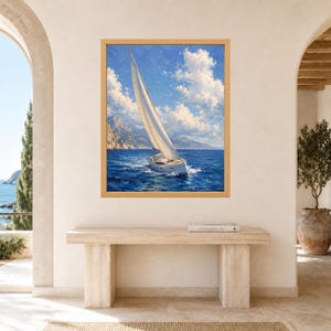 May include: A rectangular wall art print in a light wood frame depicting a white sailboat with a tall mast sailing on deep blue ocean waters under a bright sky filled with fluffy white clouds and distant rocky mountains in the background.