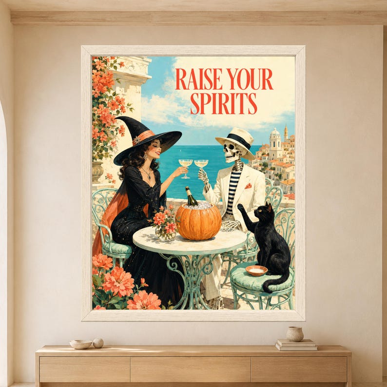 Framed Raise Your Spirits Halloween wall art featuring a stylish witch and skeleton raising cocktail glasses beside a black cat and pumpkin ice bucket on a sunny Mediterranean terrace.