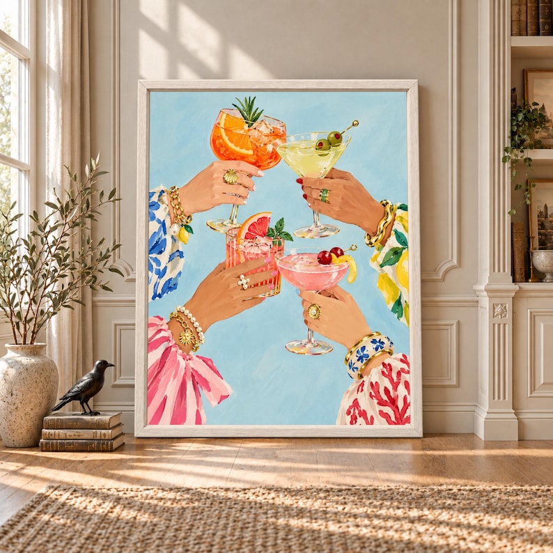 Framed colorful cocktail wall art showing four jeweled hands raising orange, yellow and pink drinks with citrus, cherries and olives against a light blue background.