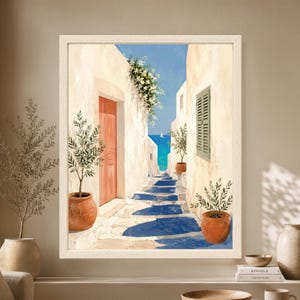 Framed Mediterranean coastal wall art showing a whitewashed stone alley with a coral door, green shutters, potted olive trees and steps leading toward a bright blue sea with a small sailboat.