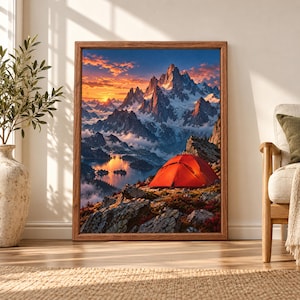 Framed mountain camping wall art showing a bright red tent on a rocky alpine ledge above a blue lake with dramatic snow-covered peaks glowing under an orange sunset sky.