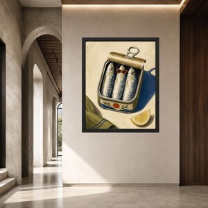 May include: A framed wall art print depicting an open metal tin of three sardines. The middle sardine wears small orange-rimmed glasses. A slice of yellow lemon sits beside the tin, and a folded green cloth with blue stripes is visible nearby.