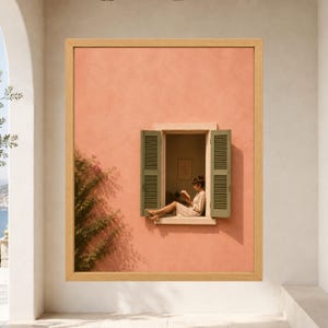 May include: A framed wall art print featuring a peach-colored stucco wall with a window. The window has open green shutters and a person sitting on the sill reading a book. A green climbing plant grows on the wall to the left of the window.