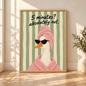 Framed funny duck bathroom wall art showing a white duck in black sunglasses, a pink robe and towel wrap beneath “5 minutes? absolutely not.” text on sage green and cream stripes.