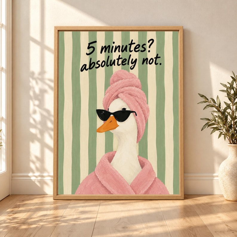 Framed funny duck bathroom wall art showing a white duck in black sunglasses, a pink robe and towel wrap beneath “5 minutes? absolutely not.” text on sage green and cream stripes.