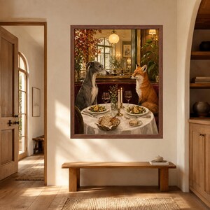 May include: A framed wall art print depicting a grey whippet and a red fox sitting at a round dining table. The table is set with white plates of food, wine glasses, candles, and a basket of bread, all within a warm, dimly lit interior setting.