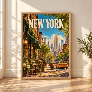 Framed New York USA travel poster showing the Empire State Building above a sunny Manhattan street with a yellow taxi, brick buildings, outdoor café tables, flowers and leafy trees.