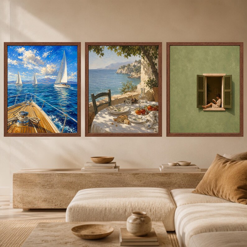 May include: A set of three framed wall art prints. The left print shows a sailboat deck overlooking the blue sea. The middle print depicts a table set for a meal on a coastal terrace. The right print features a person reading in an open window.