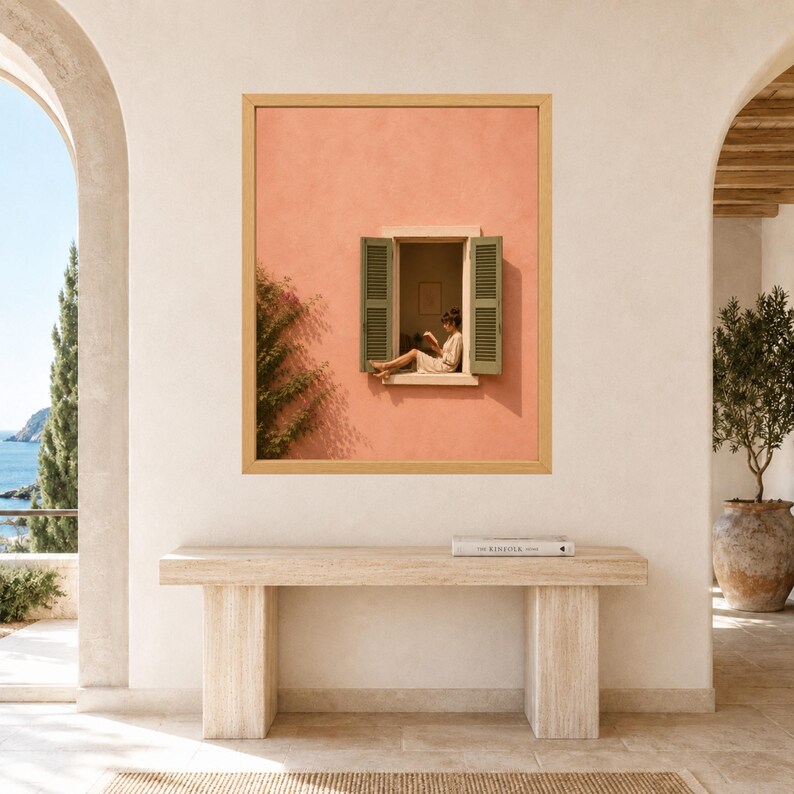 May include: A rectangular wall art print in a light wood frame featuring a peach-colored stucco wall with an open window. Green shutters flank the window, where a person sits reading a book. A climbing vine grows along the left side of the wall.