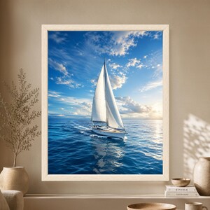 Framed sailboat wall art showing a white sailing yacht crossing deep blue ocean water beneath a wide blue sky with bright clouds and soft sunlight near the horizon.