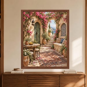 May include: A framed wall art print depicting a Mediterranean patio scene with a stone table, chairs, a patterned rug, and a stone bench. The area is decorated with pink bougainvillea flowers, terracotta pots, a hanging lantern, and an arched doorway.