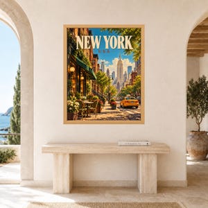May include: A framed wall art print featuring a sunny New York City street scene with the text NEW YORK USA at the top. The image displays a sidewalk cafe with green awnings, potted flowers, a yellow taxi cab, and the Empire State Building in the distance.