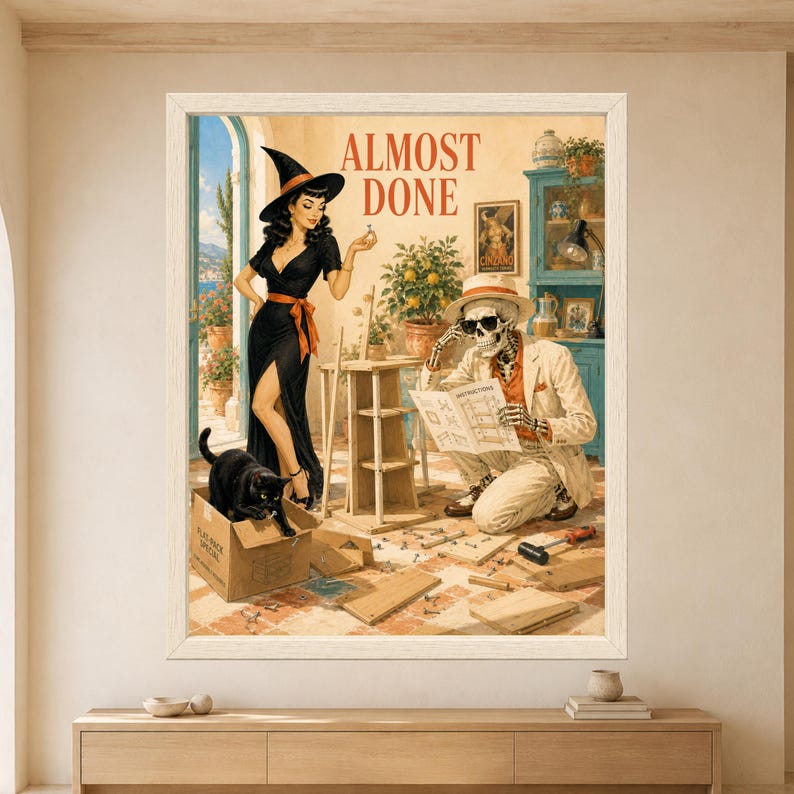 Framed Almost Done wall art showing a skeleton struggling to assemble flat-pack furniture while a retro witch holds up a leftover screw and a black cat plays inside the cardboard box.