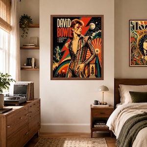 May include: A framed poster featuring a stylized illustration of David Bowie in a striped jumpsuit, with the text 'DAVID BOWIE', 'STARMAN', 'REBEL', and 'ICON' set against a vibrant background of a red lightning bolt, a moon, and a city skyline.