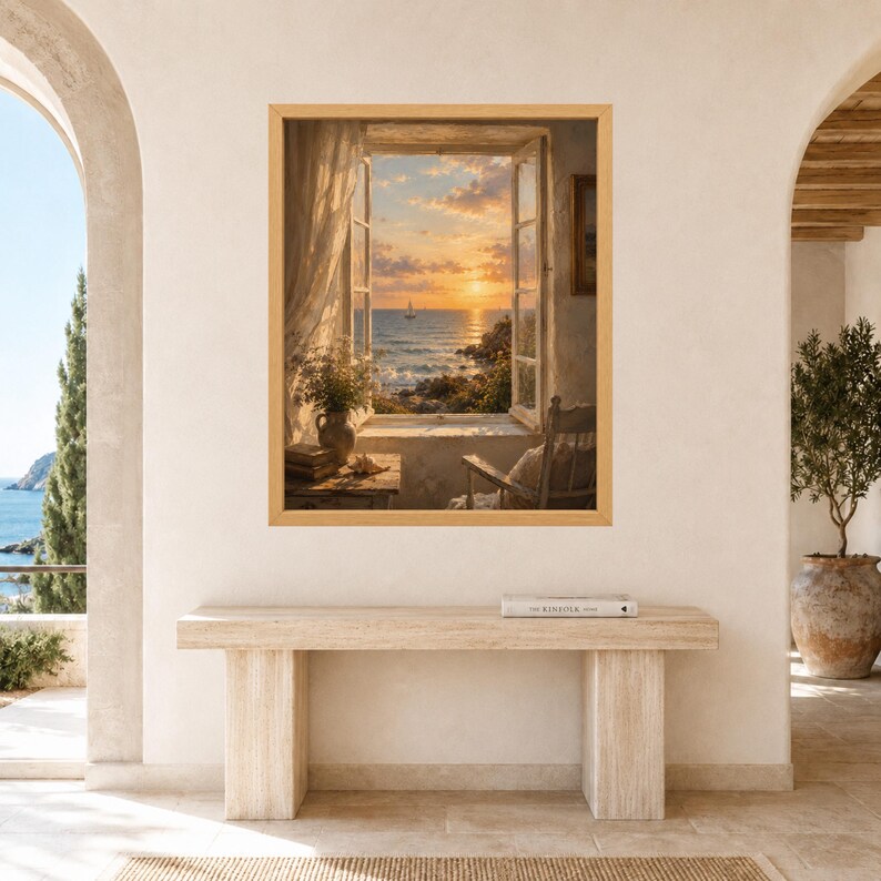 May include: A framed wall art print depicting an open window view of a sunset over the ocean with a sailboat, a wooden chair, and a small table with a vase of flowers and books, displayed above a long, rectangular, light-colored stone console table.