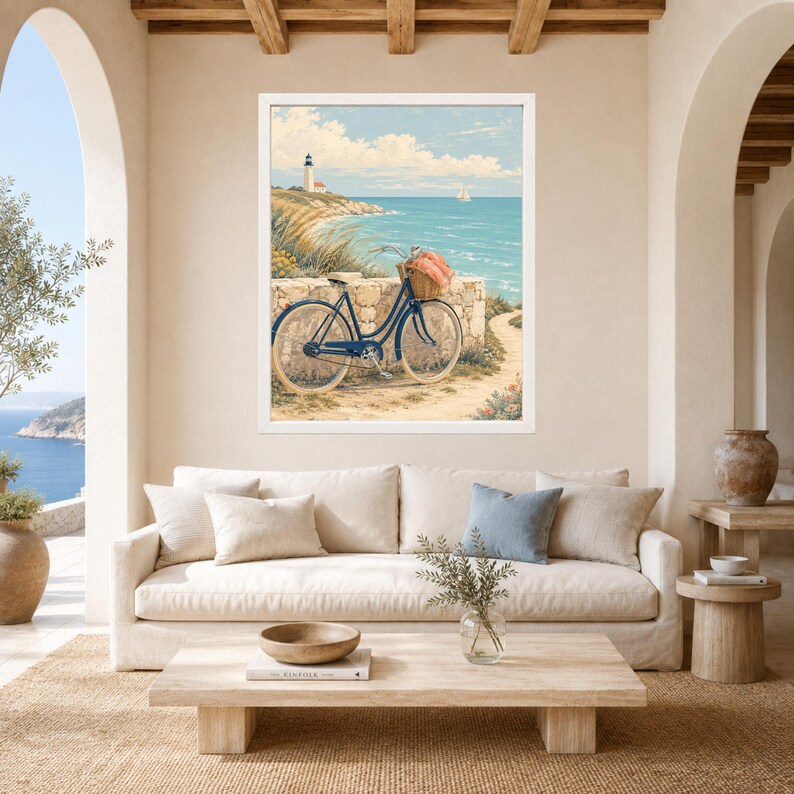 Op de afbeelding: Een ingelijste kunstdruk met een kusttafereel en een donkerblauwe fiets die tegen een stenen muur staat. De fiets heeft een rieten mand met een koraalkleurige doek. Een vuurtoren staat op een klif die uitkijkt over de blauwe oceaan.