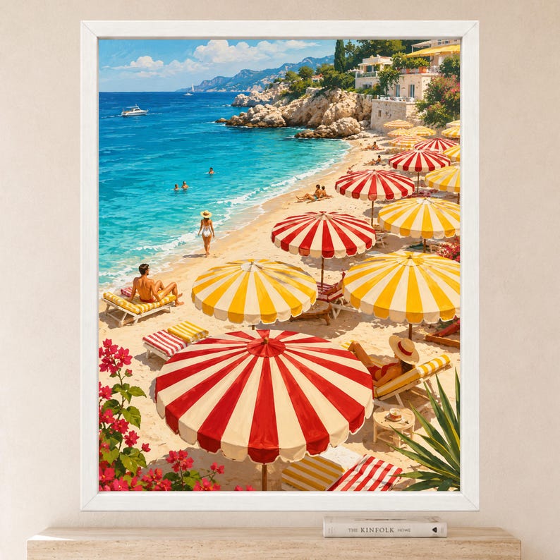 Op de afbeelding: Een ingelijste kunstdruk met een zonnig mediterraan strandtafereel met turquoise water, rotsachtige kliffen en talloze rood-witte of geel-witte gestreepte strandparasols. Mensen ontspannen op ligstoelen op het zand bij roze bloemen.