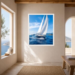 Op de afbeelding: Een ingelijste wandkunstprint met een zeilboot met een donkere romp en witte zeilen die op diepblauw oceaanwater vaart onder een heldere lucht. Het vaartuig cre&euml;ert een wit kielzog terwijl het richting verre, wazige kustbergen beweegt.