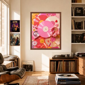 May include: A framed wall art print featuring a collage of pink, red, and white vinyl records, a pair of pink headphones, and small decorative elements like stars and flowers, displayed in a room with a record player and bookshelves.