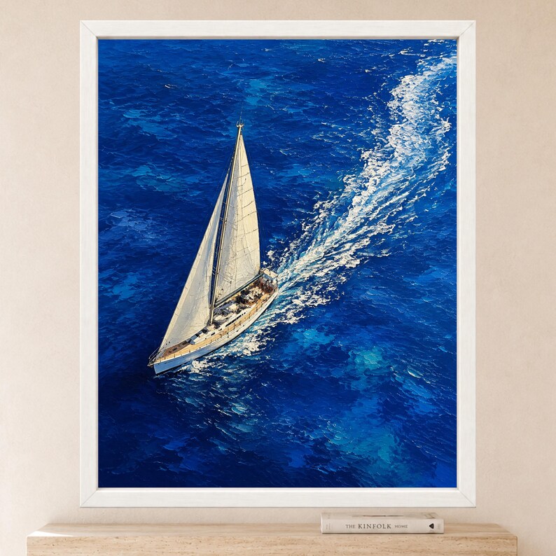 May include: A framed wall art print featuring an aerial view of a white sailboat navigating through deep blue ocean waters. The vessel leaves a prominent white wake behind it, contrasting with the vibrant, textured shades of the sea surface.