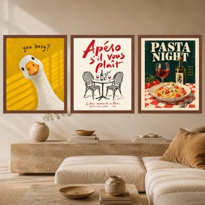 May include: A set of three framed wall art prints. The left print features a white goose on a yellow background with the text you busy?. The middle print shows a bistro table with chairs and the text Ap&eacute;ro s'il vous pla&icirc;t. The right print shows pasta.