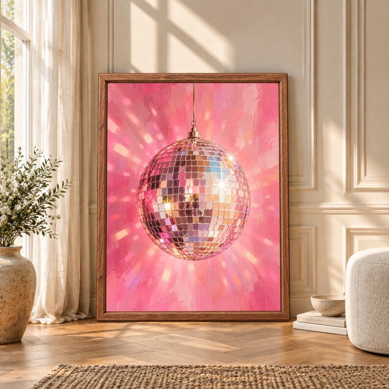 Framed pink disco ball wall art featuring a large mirrored ball reflecting silver, rose gold and pale blue light against a textured hot pink background with radiating reflections.